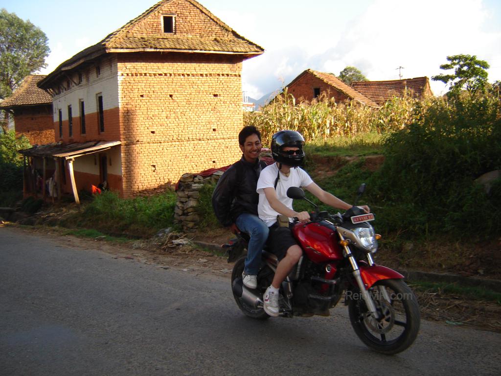 Driving Rojesh's motorcycle on the streets, with greenery and a building in the background