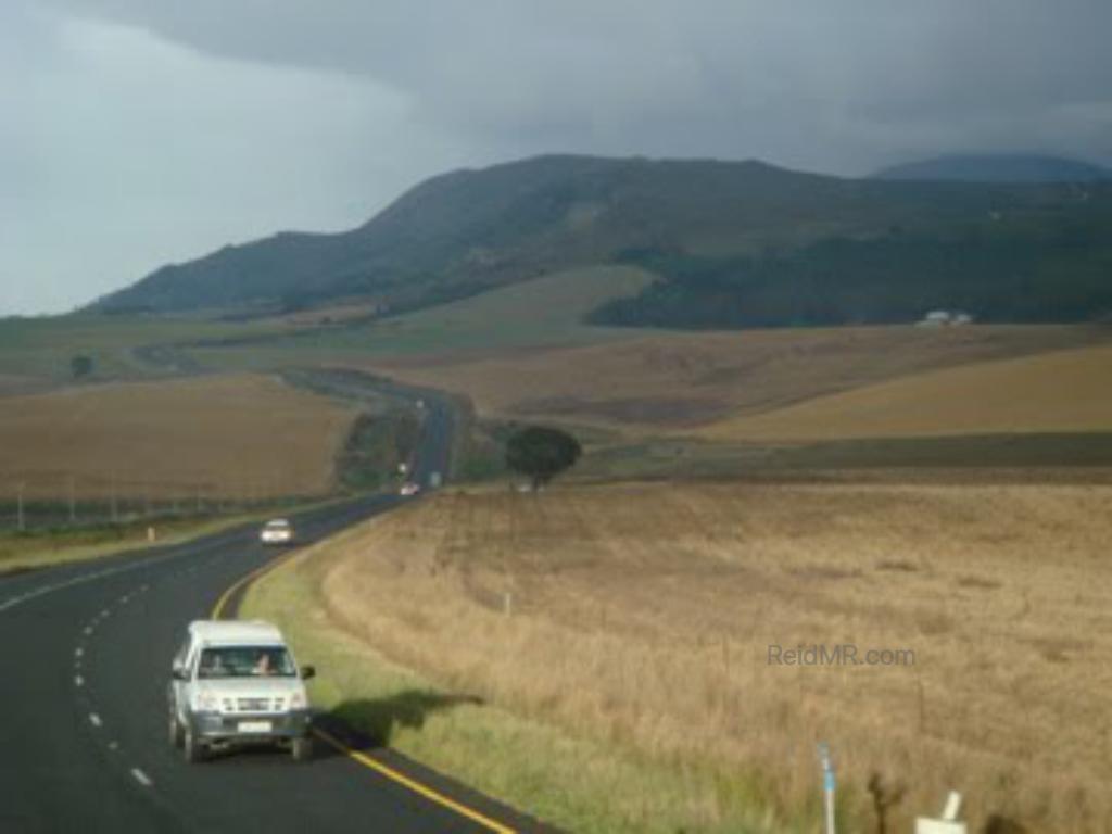 A winding road through the scenic landscape, with fields on the side and mountains in the distance.