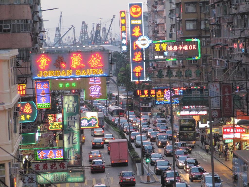 The view of a visually crowded over stimulating street in Hong Kong, with signage, wires, lights and cars. 