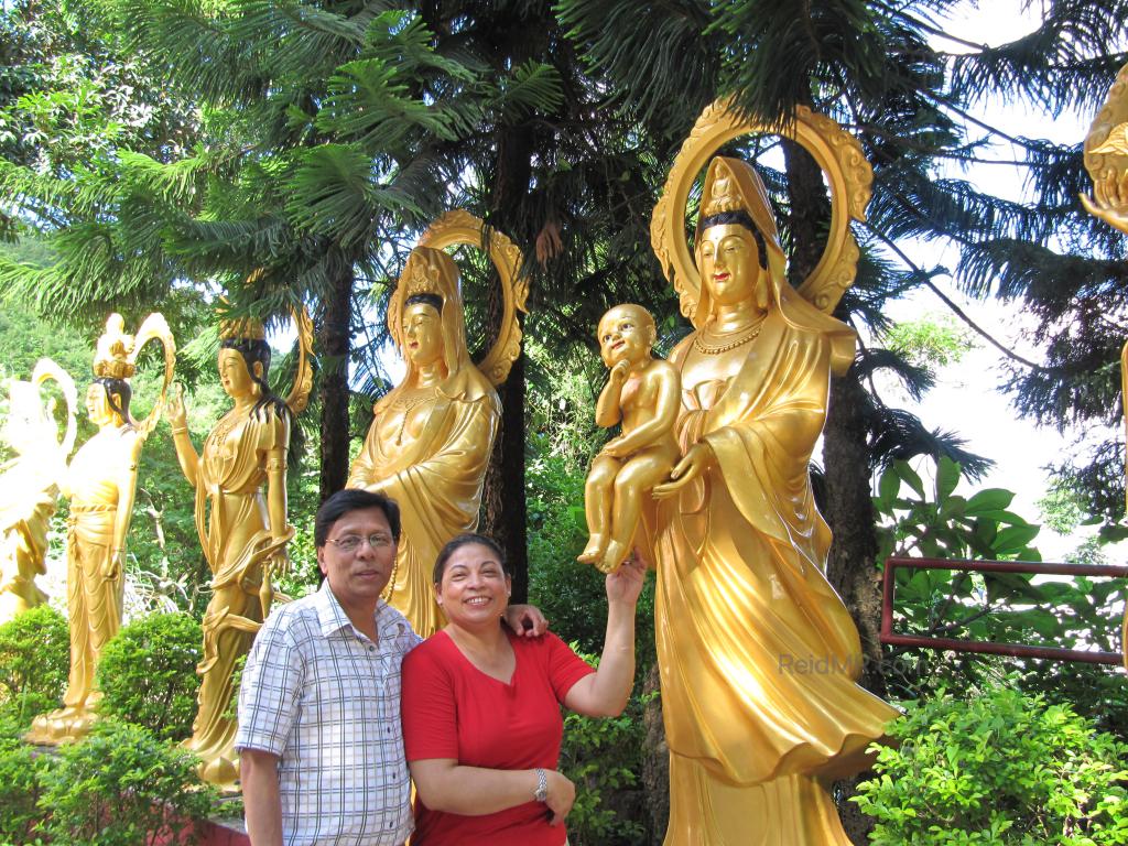 Mom and Dad with the statues in the background. She is touching the foot of a baby statue. 