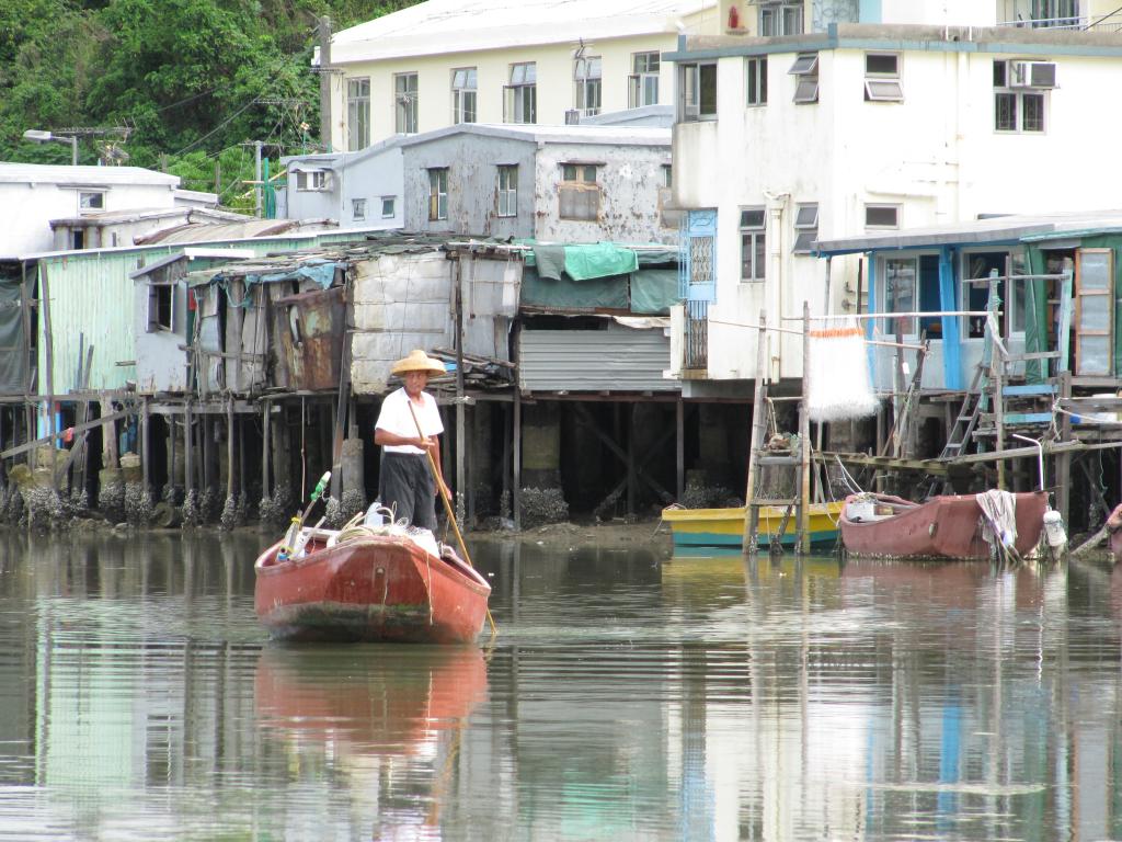 At Tai O fishing village, a man is maneuvering a boat down the river, the houses on stilts are the backdrop