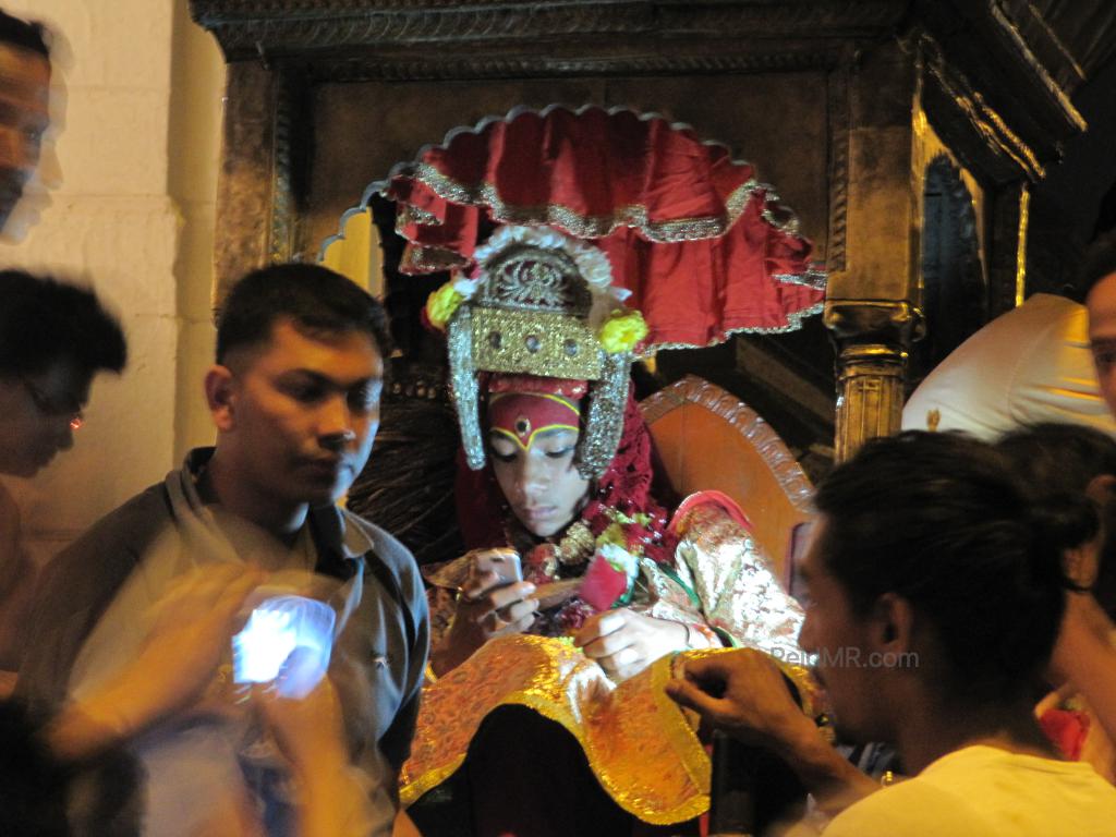 Photo of a god/goddess in Nepal. I thought it was a girl, but he is male. He is on his phone with worshippers packed around him. 