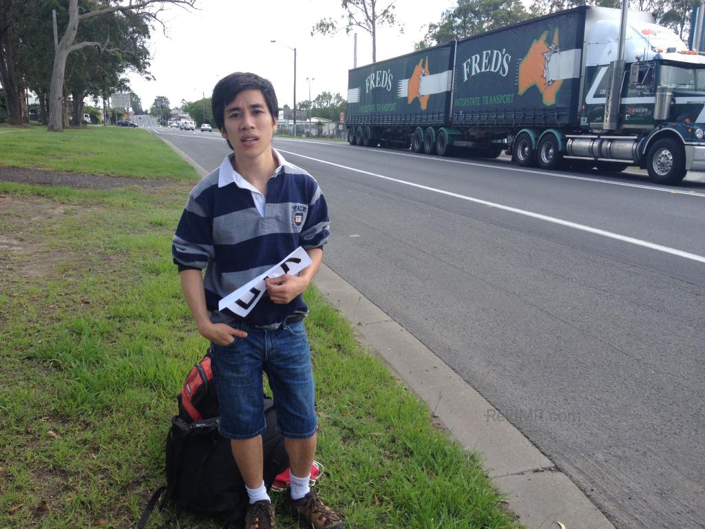 Ben on the side of the road looking unhappy with the hitchhiking sign.